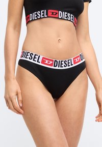 Μαύρο μαγιό μπικίνι με σχέδιο ψηλής μέσης. Η ελαστική ζώνη είναι λευκή με μαύρα γράμματα που γράφουν "DIESEL" και ένα κόκκινο λογότυπο.
