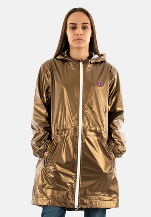 Imperméable brillant de couleur or avec capuche, fermeture éclair à l'avant, poches latérales et poignets élastiques. Présente un petit logo sur la poitrine.