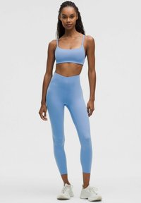 Blue sports bra and matching leggings in a smooth, stretchy fabric, featuring a seamless design and a high-waisted fit. Pairing with white sneakers.