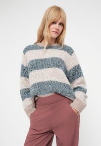 Adīts svītrots džemperis maigā bēšā, zilā un pelēkā krāsā. Ar platām svītrām, nokareniem pleciem un brīvu piegriezumu, saskaņots ar rozā biksēm.