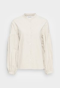 Vaaleanbeige nappipaita, jossa on korkea kaulus, runsaat hihat ja kerätyt hihansuut, valmistettu pehmeästä, teksturoidusta kankaasta.