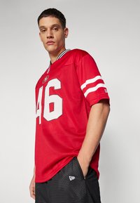 Piros sportme shortsleeves-tartalmazó póló, fehér csíkokkal és hálós textúrával. A 46-os szám jól láthatóan szerepel az elején.