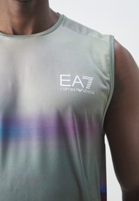 T-shirt de sport sans manches gris avec un dégradé violet et le logo EA7 Emporio Armani sur la partie supérieure de la poitrine porté par une personne.