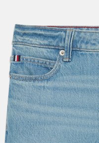 Světle modré denimové džíny s přední kapsou a červeným, bílým a modrým pruhem. Klasický design s pěti kapsami, volný střih.