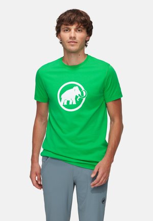 Groene katoenen T-shirt met een witte olifantenafbeelding binnen een cirkel. Korte mouwen en ronde hals, gecombineerd met grijze broek.