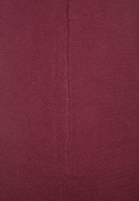 Tessuto a maglia bordeaux con una superficie liscia e un dettaglio centrale di cucitura. Il materiale è elasticizzato e aderente.