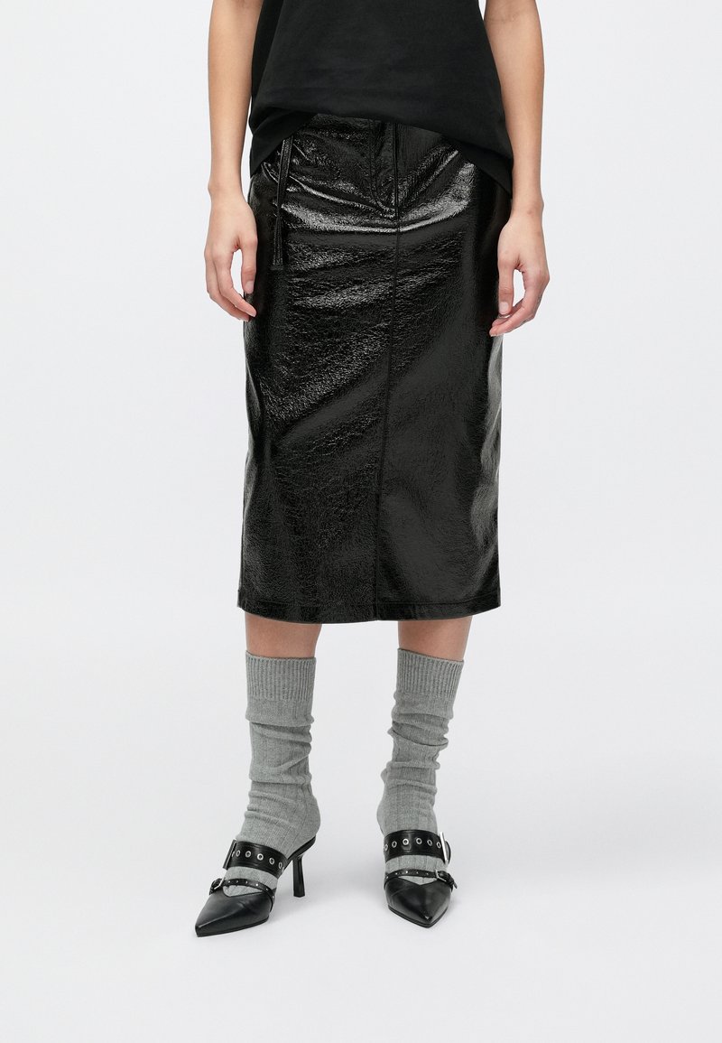 Juoda, blizgi odinė midi sijonas su priekyje esančia užtrauktuku ir siūlių detalėmis. Derinama su pilkomis kelių ilgio kojinėmis ir juodais aukštakulniais su dirželio akcentais.