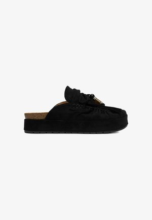 Mule slip-on de ante negro con suela gruesa, lazo decorativo y adornos de cuentas en la parte superior, mostrado de perfil.