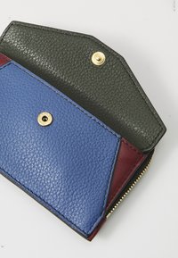 Portefeuille en cuir tricolore avec une section bleue texturée, un intérieur vert foncé et une touche maroon. Il possède une fermeture à bouton-pression doré et une fermeture éclair.