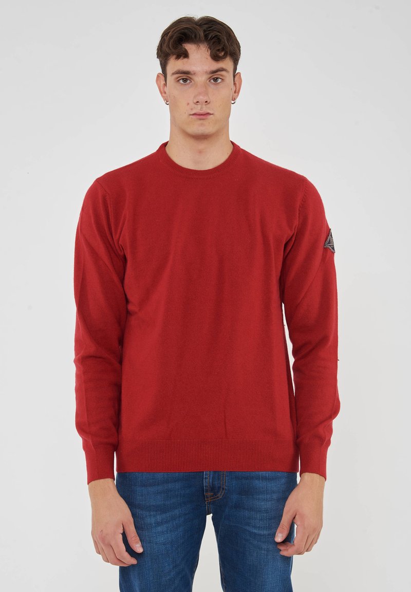 Maglione rosso a maglia con maniche lunghe e scollatura rotonda. Presenta un tessuto texturizzato e una toppa con logo sulla manica sinistra.