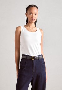 White tank top made of soft fabric, paired with high-waisted dark blue trousers featuring a thick black belt and gold buckle.