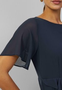 Marineblauwe jurk met korte, luchtige mouwen en een aansluitend bovenstuk met een geplooide taille. Glad textiel met een subtiele glans.