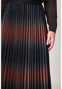 Jupe plissée noire avec un effet ombragé passant du noir à l'orange rouge. Elle dispose d'une large ceinture et d'une finition texturée.