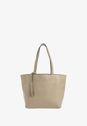 Sac fourre-tout en cuir beige avec deux poignées de transport, détail en forme de pompon et trois clous décoratifs à l'avant. Design simple et structuré.