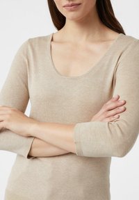 Beżowy sweter z dekoltem w serek i rękawami do łokci, wykonany z miękkiej tkaniny, o gładkiej fakturze i dopasowanym kroju.