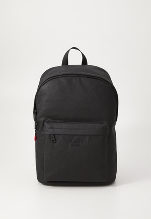 Schwarzer Stoffrucksack mit einem oberen Griff, gebogenen Reißverschluss, Fronttasche und Logodetail. Glatte Textur und minimalistisches Design.