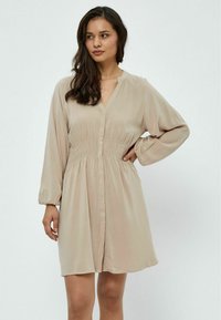 Vestito beige con bottoni realizzato in un tessuto morbido e leggero. Presenta una vita arricciata, maniche a palloncino e scollatura a V.