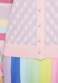 Pastellfärgad cardigan med ett diamantmönster i ljuslila och rosa, med pärlknappar och ribbade muddar, i kombination med en flerfärgad randig kjol.