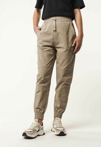 Lichtbeige broek met een elastische tailleband en zijzakken. Gemaakt van een gestructureerde stof met geschalde mouwen, gecombineerd met witte en beige sneakers.