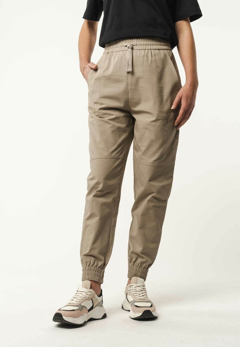 Lichtbeige broek met een elastische tailleband en zijzakken. Gemaakt van een gestructureerde stof met geschalde mouwen, gecombineerd met witte en beige sneakers.