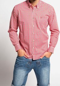 Chemise à carreaux vichy rouge et blanc avec col boutonné et manches longues. Dotée de boutons dorés et portée avec un jean en denim bleu.