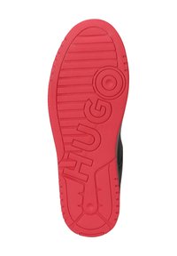 Semelle de sneaker noire avec un important caoutchouc rouge en dessous, présentant des rayures texturées et un détail de logo arrondi qui indique "HUGO".