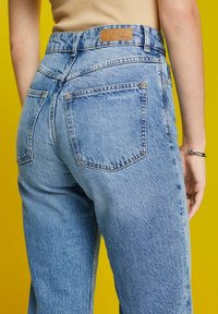 Jeans de mezclilla azul claro con una cintura alta, piernas rectas y dos bolsillos traseros. Presenta un parche de cuero marrón en la cinturilla.