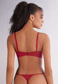 Spitzenunterwäscheset in tiefem Rot, mit verstellbaren Trägern, gewellten Kanten und einem minimalistischen Tanga-Stil mit filigranen Blumenmustern.