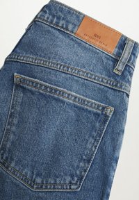 Poche arrière et ceinture en denim bleu avec des coutures visibles et une étiquette de marque en cuir marron portant l'inscription « MNG Authentic Denim ».