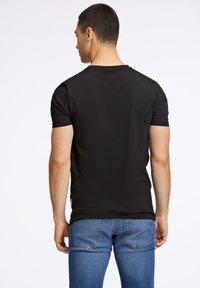 Czarny bawełniany t-shirt z krótkim rękawem, okrągłym dekoltem i dopasowanym krojem, w połączeniu z niebieskimi dżinsami z kontrastowym przeszyciem.