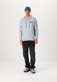 Grå hættetrøje med en front kangaroo lomme, snoretræk i hætten og logo detaljer. Stylet med sorte jeans og grå sneakers.