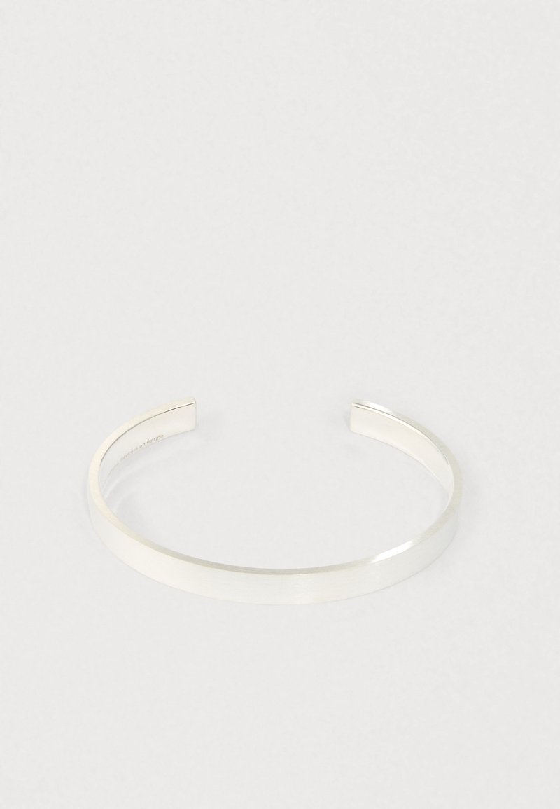 Brățară minimalistă din argint, cu suprafață netedă și lustruită, expusă pe un fundal deschis simplu, cu un design deschis la capete.