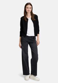 Zwarte, gestructureerde cardigan over een wit t-shirt, gecombineerd met hoge, wijde donkere spijkerbroeken en witte sneakers. Eenvoudige, casual outfit.