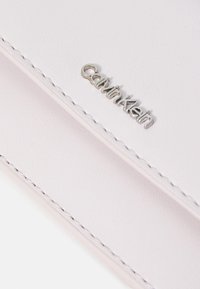 Peňaženka Calvin Klein z mäkkej, svetloružovej ekologickej kože so strieborným logom a úhľadným prešívaním. Hladký povrch a štíhly, obdĺžnikový tvar.