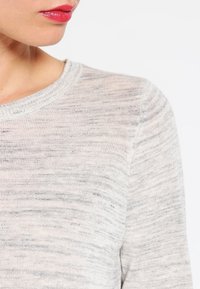 Jasnoszary, miękki sweter dzianinowy z okrągłym dekoltem i subtelną fakturą. Posiada lekko melanżowy wzór, tworzący delikatną głębię wizualną.