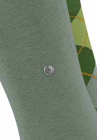 Zwei Paar Socken: eines in einfarbigem hellgrün mit strukturierter Oberfläche, das andere mit einem dunkelgrünen Argyle-Muster und orangefarbener Naht.