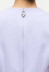 Φόρεμα σε λιλά απόχρωση με απαλή υφή, στρογγυλή λαιμόκοψη και ασημένια κυκλική διακοσμητική λεπτομέρεια στην πλάτη, με κεντρική ραφή.