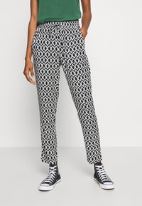Pantalon à motifs noir et blanc avec taille à cordon, coupe ajustée et longueur à la cheville, associé à des baskets montantes noires.