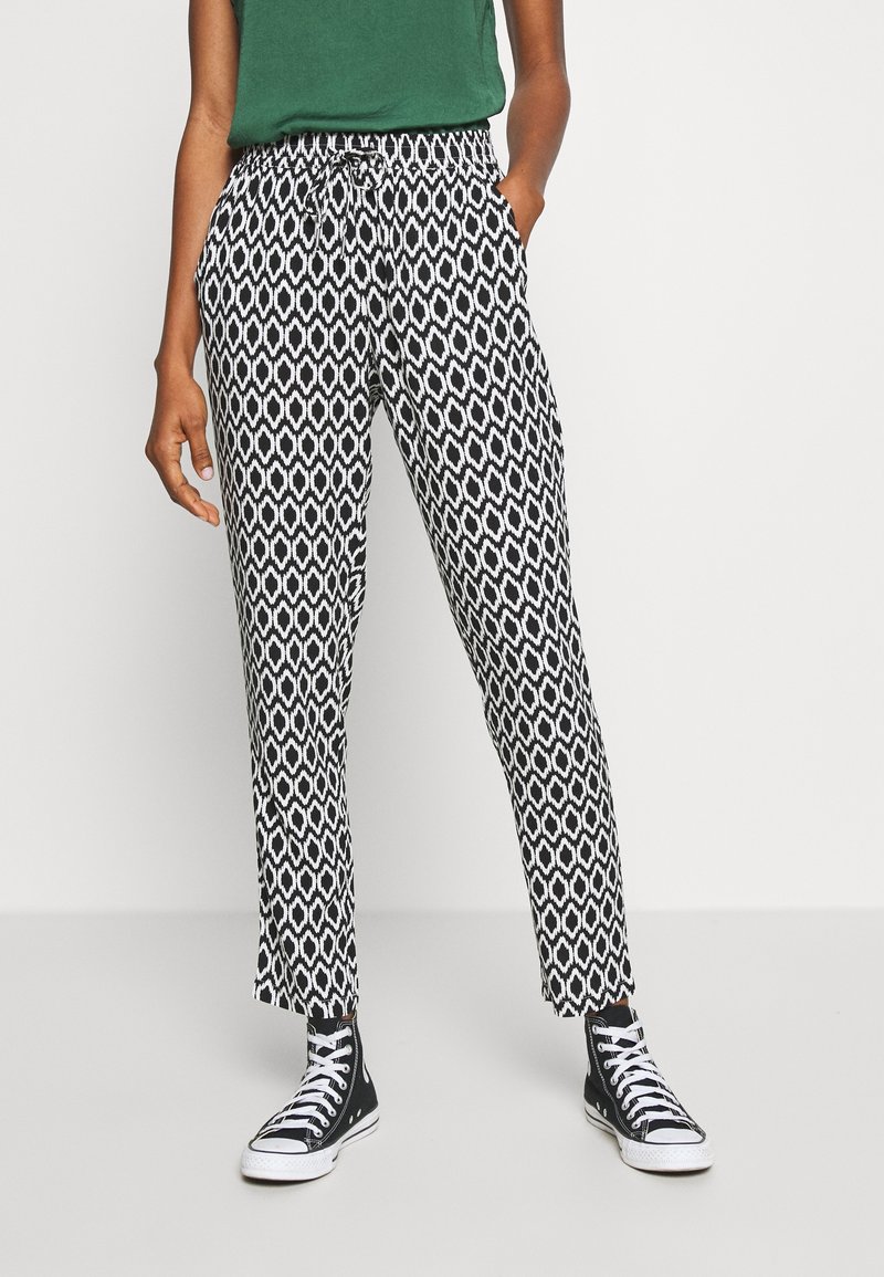 Pantalon à motifs noir et blanc avec taille à cordon, coupe ajustée et longueur à la cheville, associé à des baskets montantes noires.