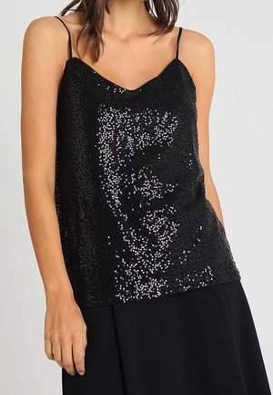 Mujer con un top negro sin mangas con lentejuelas, tirantes finos y un sutil escote en V, combinado con una falda negra sobre un fondo liso.