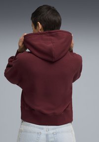 Bordeaux hættetrøje med en tekstureret overflade, justerbar hætte og ribbet kant, parret med lyseblå høj talje jeans.