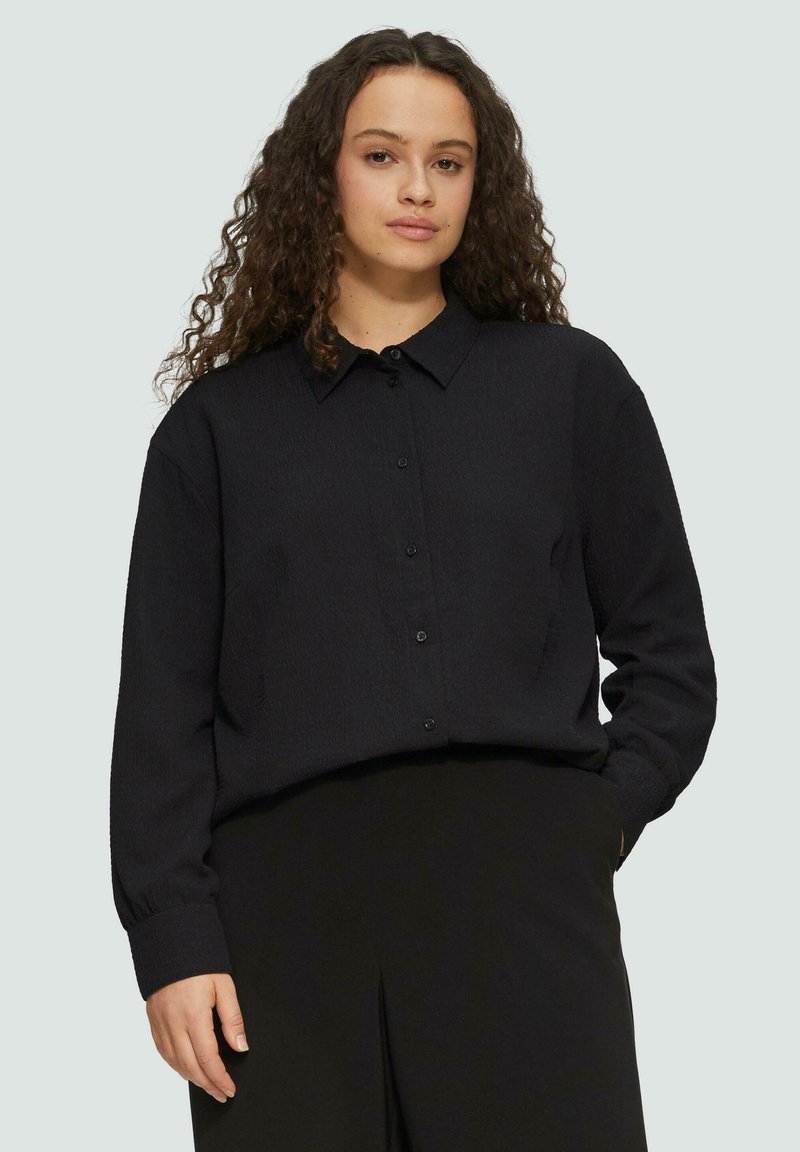Zwarte button-up shirt van een textuurstof, met lange mouwen en een kraag. Heeft een recht model en is gecombineerd met zwarte broeken.