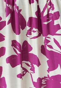 Tekstiil, millel on suured julged lillakad lillemustrid kreemjal taustal, veidi tekstuurse pinnaga ja kergelt voltis riide välimus.
