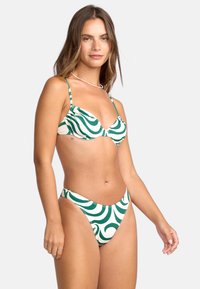 Bikinitrupp med ett grönt och vitt vågmönster, tillverkad av elastiskt tyg. Toppen har justerbara remmar och en kupa design.
