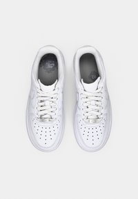 Pair of white Nike Air Force 1 sneakers with laces, perforated toe area, and cushioned collars, viewed from above on a light background.
