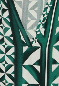 Grüner und weißer, gemusterter Stoff mit geometrischen Designs, die scharfe Winkel und verschiedene Farbtöne zeigen, sowie einem tiefen V-Ausschnitt.