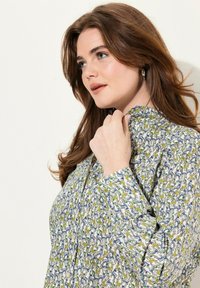 Blusa de manga larga con una tela blanca que presenta un colorido patrón de animales y plantas. Incluye botones y un escote ligeramente fruncido.