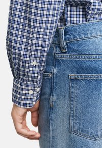 Camisa de cuadros azul y blanca con botones blancos, combinada con unos vaqueros de denim azul claro que presentan un diseño clásico de cinco bolsillos.