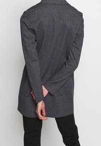 Tumma harmaa kuvioitu takki, joka on muotoiltu ja siinä on kaulus, suora leikkaus ja pitkät hihat. Tasainen pinta ilman näkyviä varusteita.