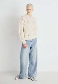 Kremfarget kabelstrikket cardigan med knappelukking, prydet med paljettdetaljer. Kombinert med lyseblå vide jeans og sølvfargede slip-on sko.